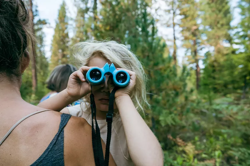 A child looks through binoculars while in their parents arms on a walk at the Metolius Preserve.